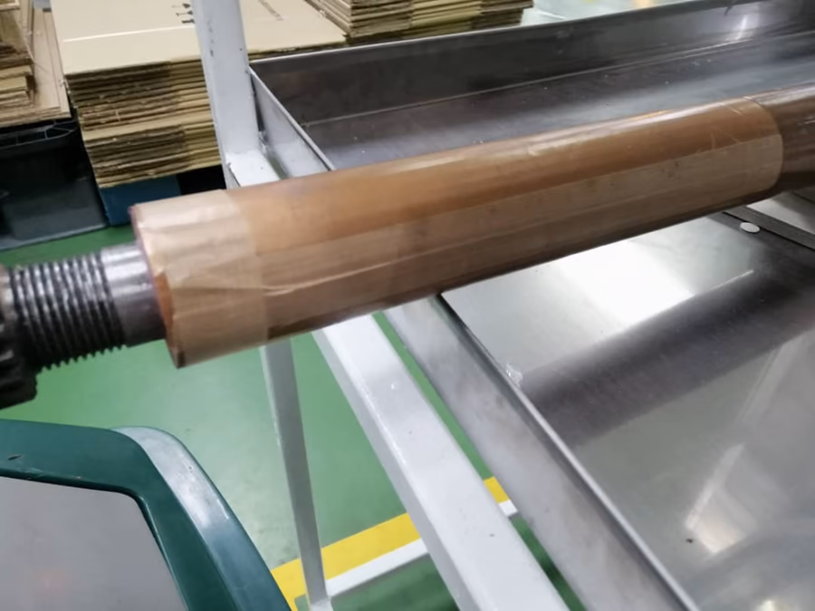Steel roller being wrapped with brown PTFE Cloth Tape without liner.
